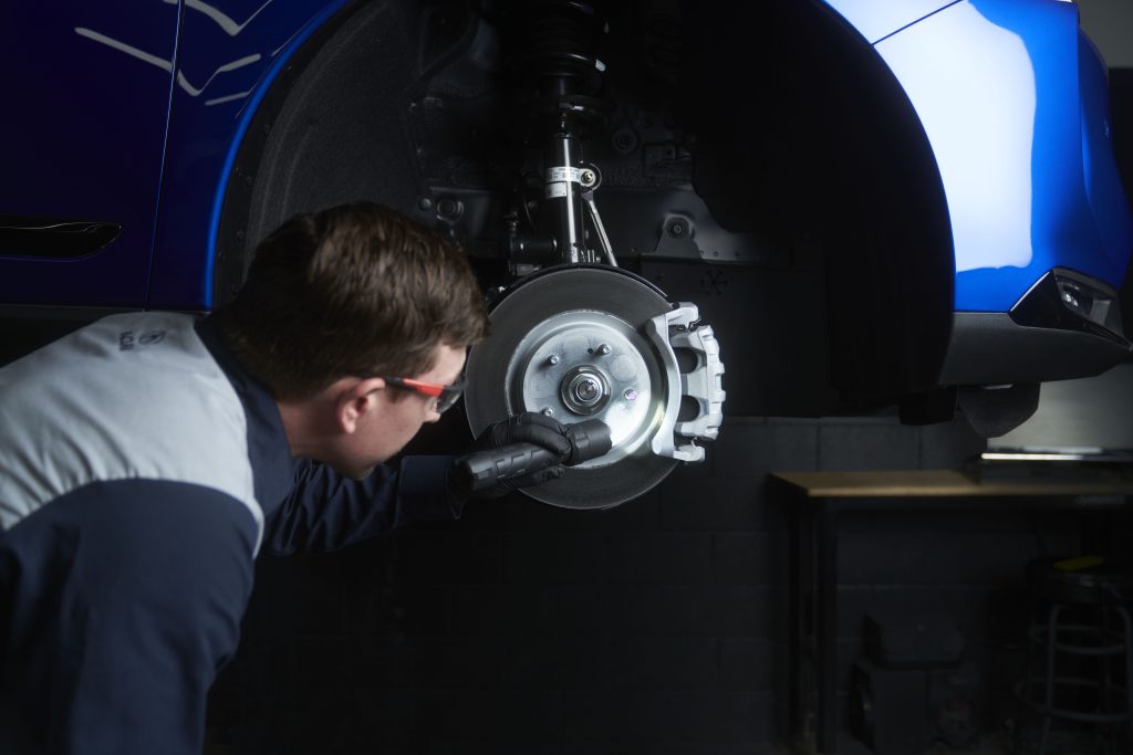 Technician inspecting a vehicle's brake rotor and caliper assembly during a professional brake service.