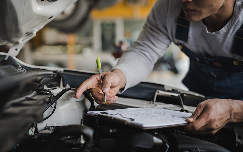 Service technician inspecting a vehicle engine and documenting findings during a professional maintenance inspection.